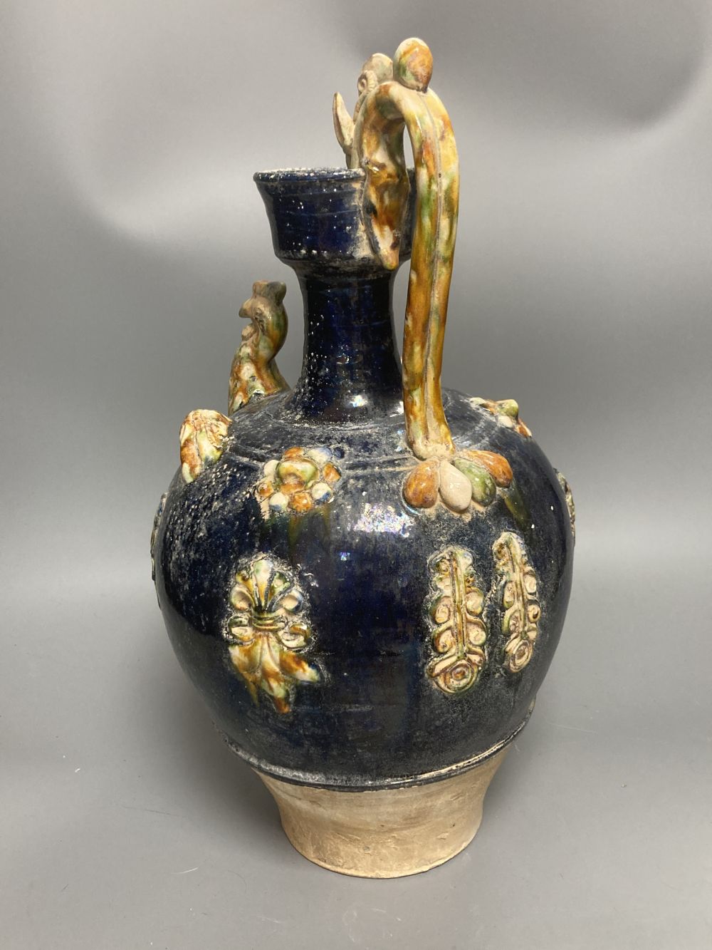 A group of Chinese Tang style pottery figures, tallest 28cm and a partially glazed ewer in sancai colours against a blue ground, 40cm